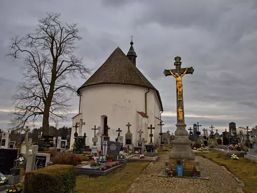 Bílá kaple na hřbitově s kříži pod šedou oblohou