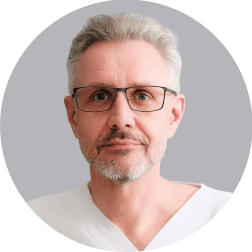 Muž s brýlemi a šedou vousy na neutrálním pozadí.