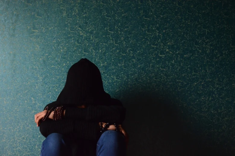 Hooded person hugging knees