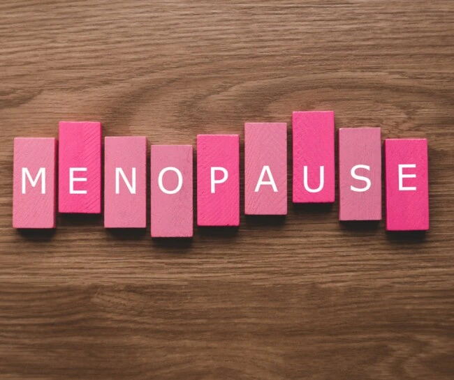 Růžové dřevěné kostky s písmeny tvořící slovo menopauza na dřevě.