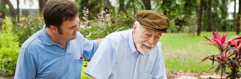 Mladý muž pomáhá staršímu muži chodit venku.