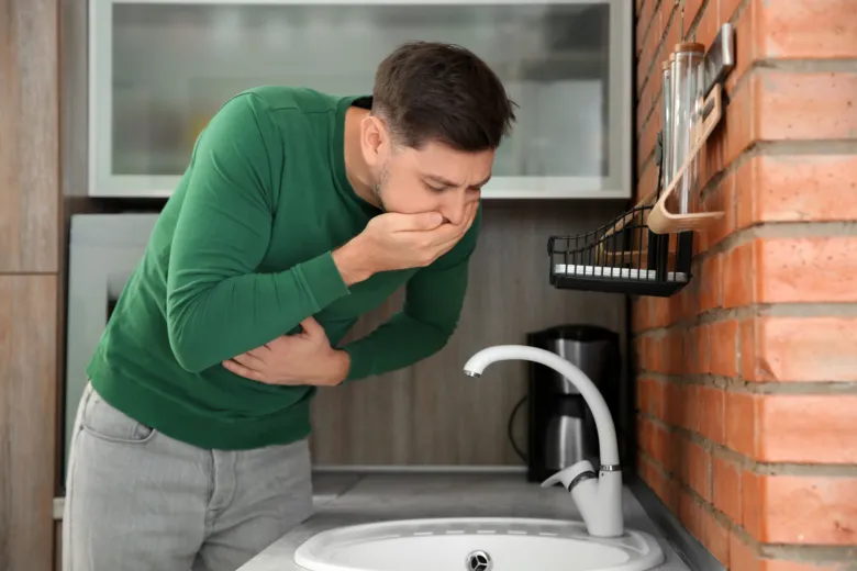 Muž se cítí nemocný v kuchyni s rukou na břiše.