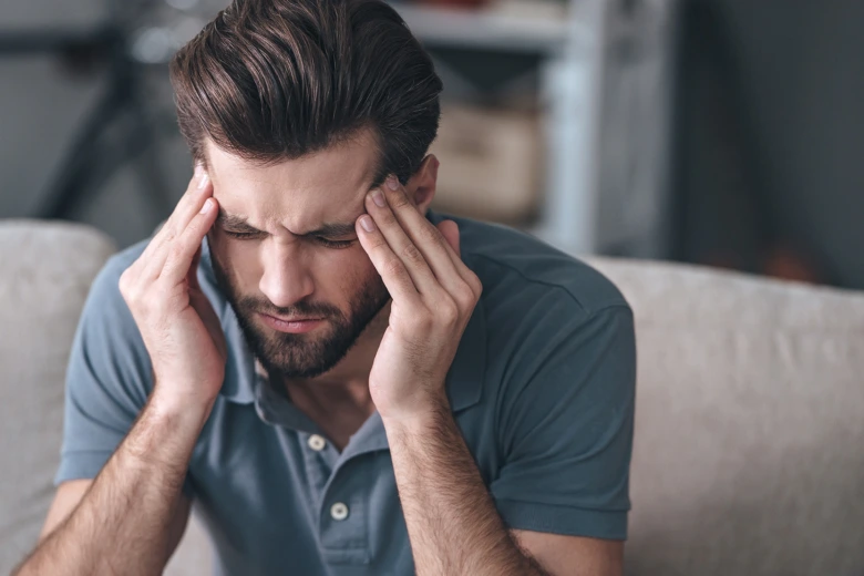 Muž drží hlavu rukama kvůli psychosomatické bolesti.