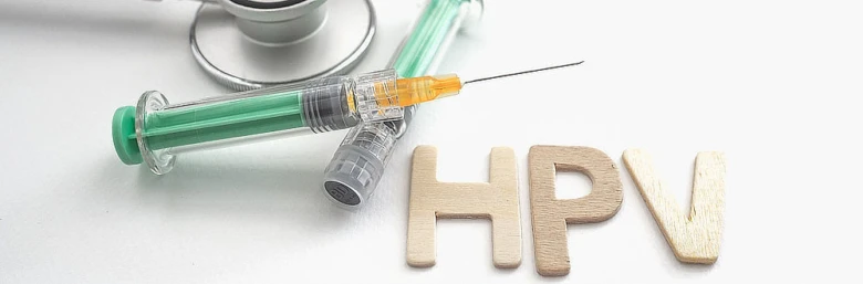 Střiková jehla s vakcínou proti HPV vedle dřevěných písmen.