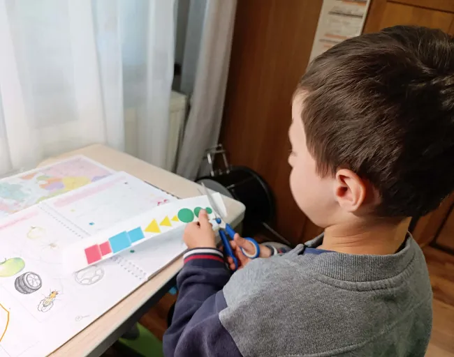Dětský chlapec řezá barevné tvary z papíru.