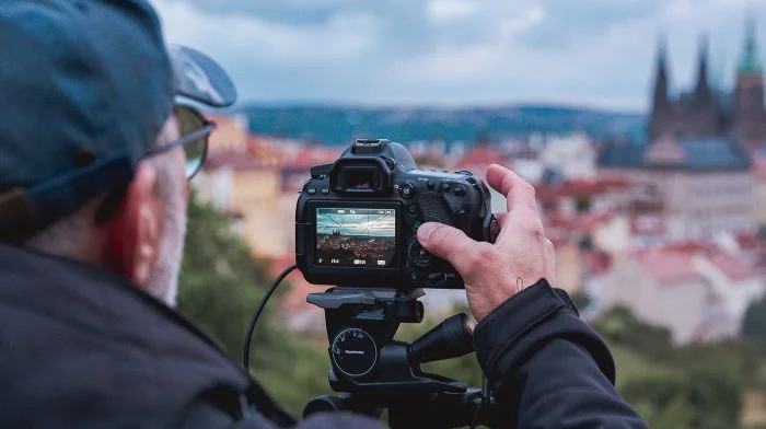 Fotograf s fotoaparátem na stativu před městem.