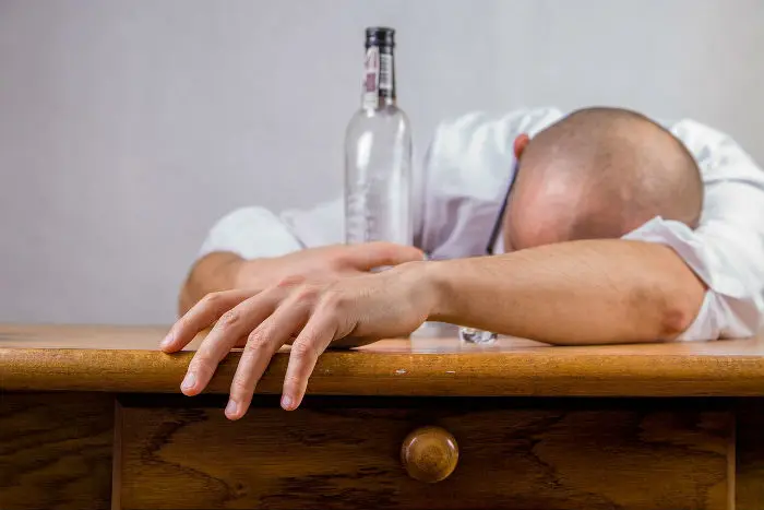 Muž leží na stole vedle prázdné láhve alkoholu.