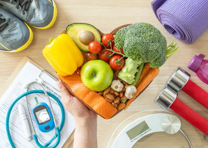 Ruka drží srdcovitý salát zdravé potravy a fitness pomůcky.