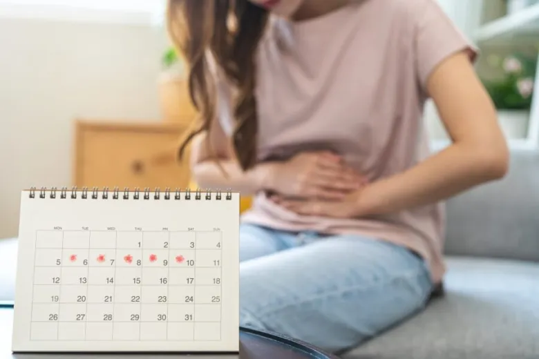 Žena drží břicho s kalendářem označujícím menstruační dny pro PMS.