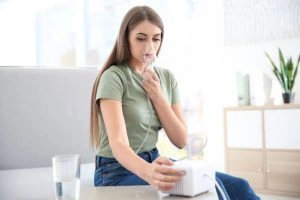 Žena používá inhalátor v domácnosti pro léčbu dýchacích cest.