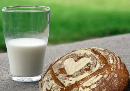 Sklenice mléka s chlebem na kamenném povrchu venku.