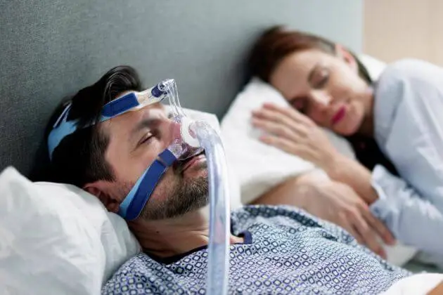 Muž spí s přístrojem na léčbu syndromu spánkové apnoe.