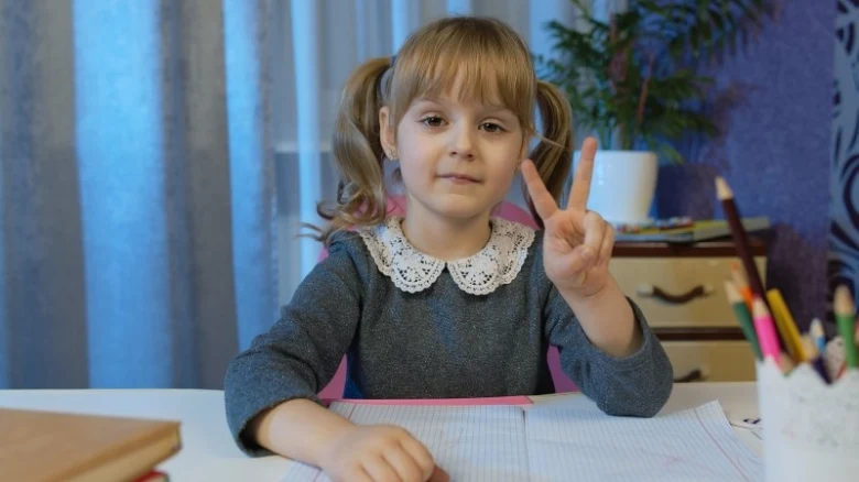 Malá dívka sedí u stolu s papírem a dává pět prstů.