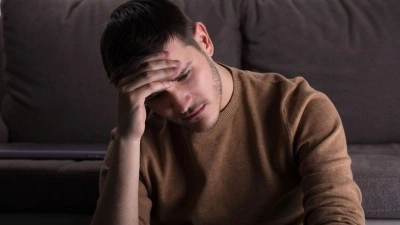 Muž sedí v zoufalství s rukou na čele.