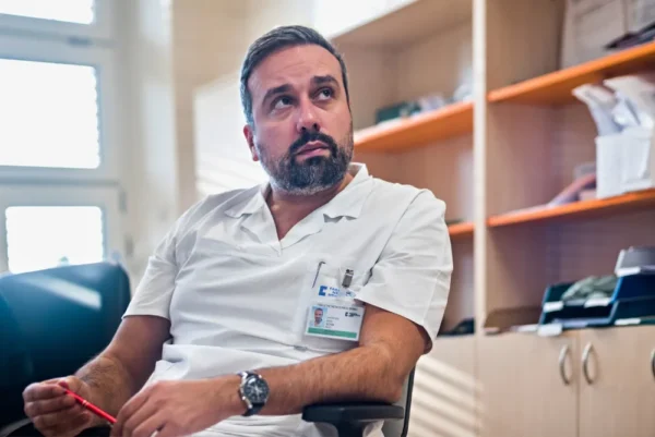 Muž v bílé košili sedí s tužíčkou v ruce.