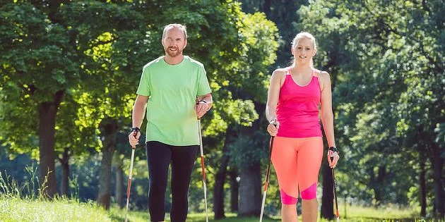 Dva lidé chodí venku s hůlkami pro nordic walking.