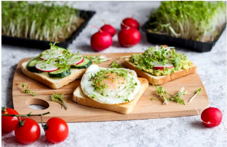 Tři toasty s řeřichou z ředkvičky na dřevěném talíři.