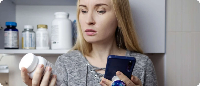 Žena v kuchyni kontroluje doplňky stravy na mobilu.