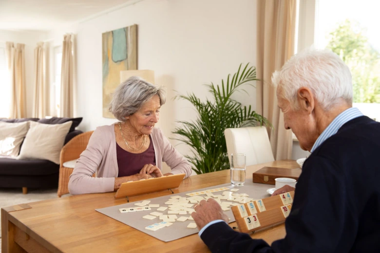 Dvojice seniorů hraje společně hru na paměť v obývacím pokoji.