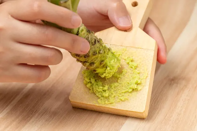 Rozdírání čerstvého kořene wasabi na dřevěné desce.