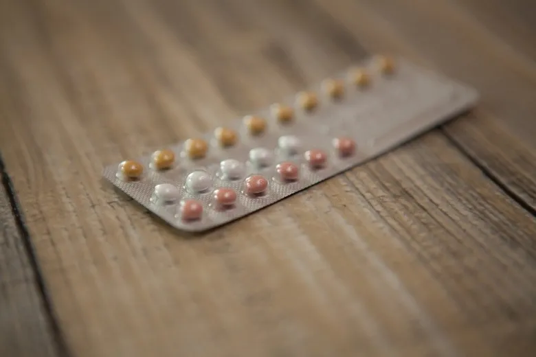 Blister s tabletkami na hormonální antikoncepci ležící na dřevě.