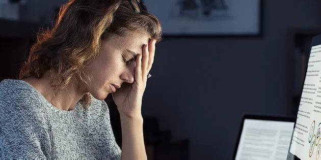 Unavená žena sedí u počítače s rukou na čele.
