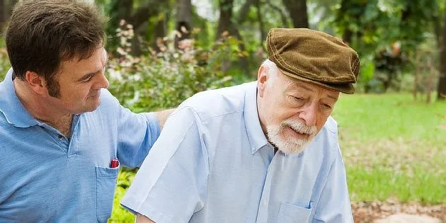 Starší muž s oporou v zahradě, příznaky Parkinsonovy nemoci.