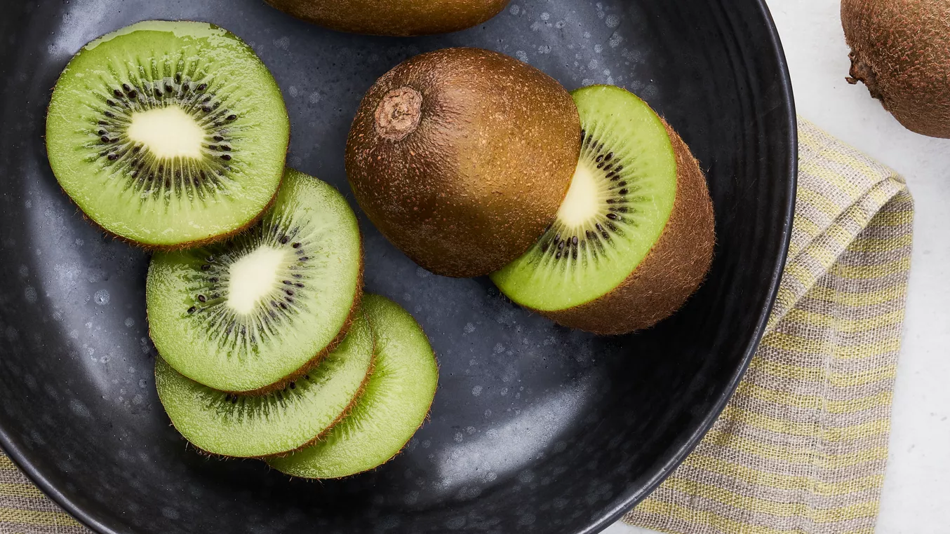 Černá miska s celými a nakrájenými zelenými kiwi.