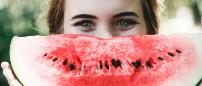 Žena drží kus vodní melounu před tváří s viditelnými zrny.