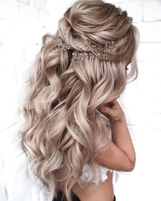 Nevěstina dlouhá vlnitá blond vlasy s květinovým doplňkem.