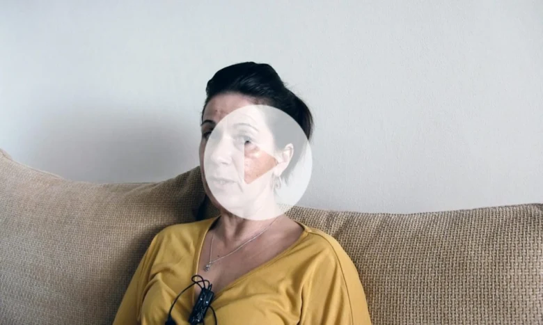 Žena sedí na gauči v žlutém tričku s neutrálním pozadím.