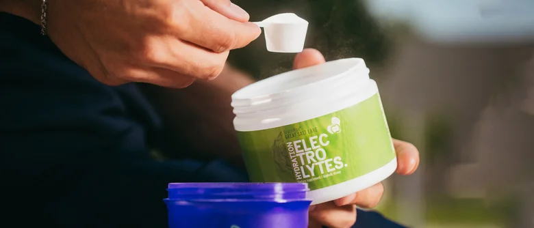 Osoba měří elektrolytový prášek do šálku pro hydrataci.
