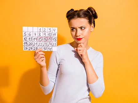 Žena drží kalendář s červeně zvýrazněnými dny menstruace.