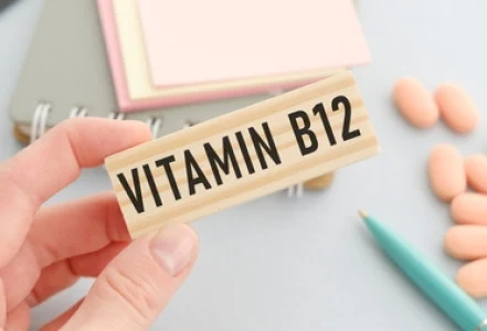 Ruka drží dřevěnou tabuli s nápisem Vitamin B12 vedle tablet.