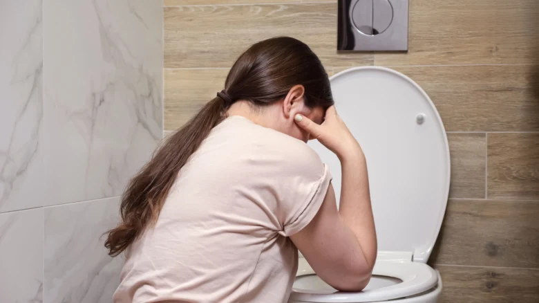 Žena sedí na záchodě s příznaky nevolnosti.